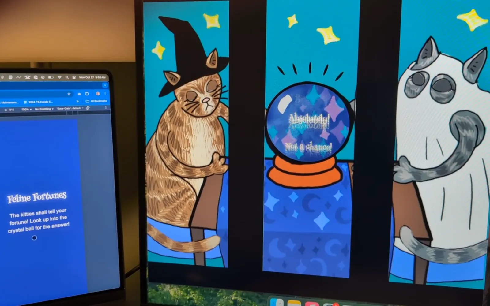 The Feline Fortunes projection on a monitor: a tabby cat in a witch’s hat on the left, a crystal ball in the centre showing the answer “Absolutely!”, and a wide-eyed grey and white cat on the right, with the phone interface open on a laptop alongside.